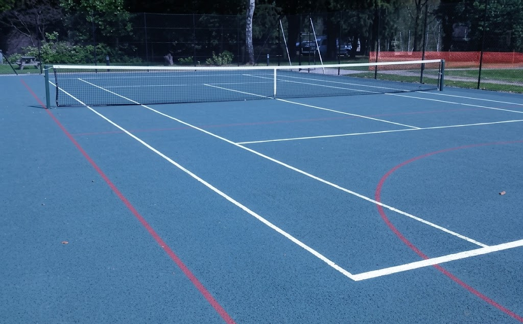Outdoor tennis court with a blue surface, white and red boundary lines, surrounded by a green fence