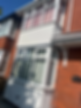 Low angle view of a red brick house exterior with white bay windows and a white facade panel under a blue sky