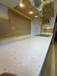 Speckled white countertop under a cabinet with lights, surrounded by protective brown paper and yellow tape