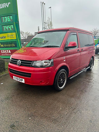 A red Volkswagen van is parked at a gas station on a rainy day