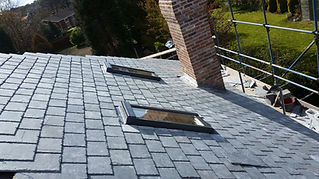 A slate-tiled roof with two skylights next to a brick chimney.