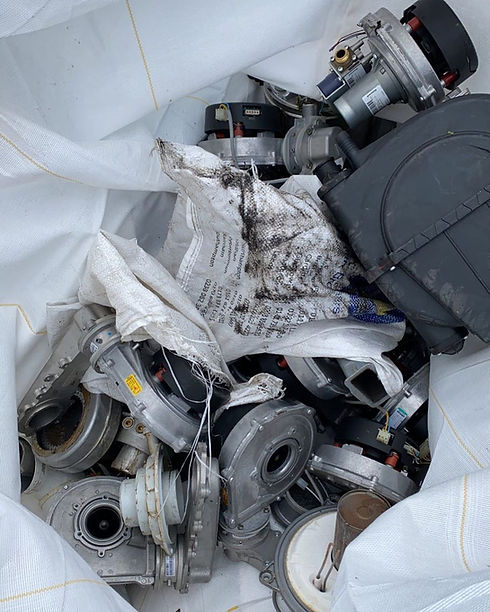A bag filled with assorted metal machine parts, featuring gears and motors, resting on a white fabric