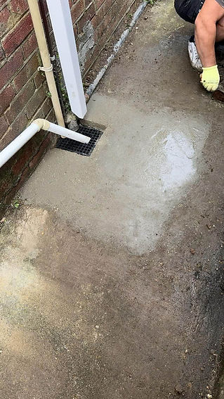 A wet concrete surface with a small puddle next to a drainage