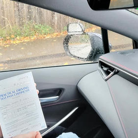 Young man in a car holding a sheet of paper smiling proudly