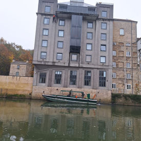 A gray multi-story building stands beside a calm river