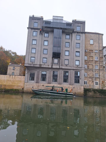 A gray multi-story building stands beside a calm river