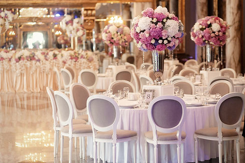 Luxurious wedding reception hall with round dining tables, elegant chairs and tall pink and white floral centerpieces