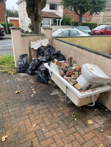 Pile of black and white bin bags dumped on a residential pavement next to a low brick wall
