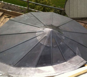 A conical, gray metal roof viewed from above, featuring triangular panels converging at the peak