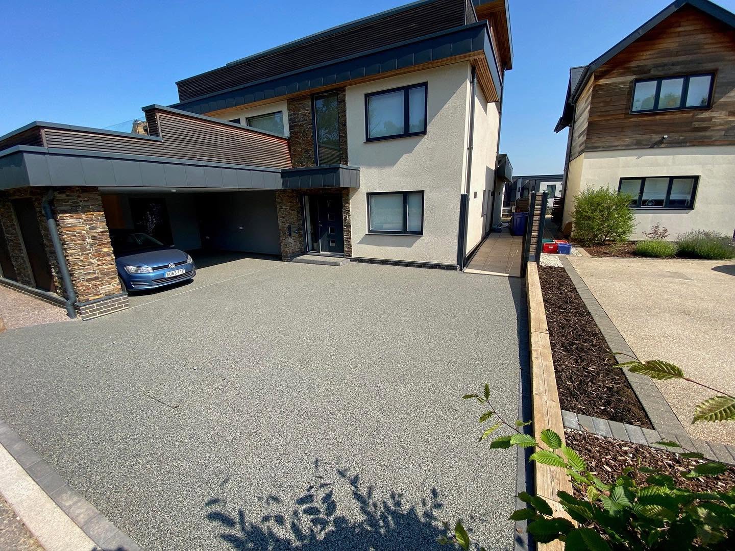 Wide light grey gravel driveway leading up to a large modern detached family house