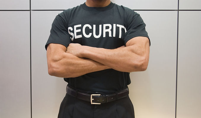 Close up of a security guard wearing a black security t-shirt with arms crossed at a venue entrance