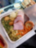 A foil tray contains a hearty meal of sliced ham and beef, peas