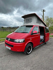 Red Volkswagen campervan parked on a road with its side door open and pop-up roof extended