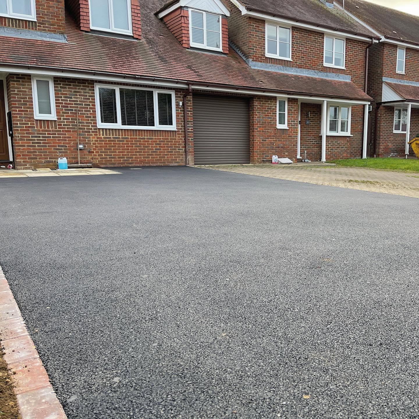 Large newly laid tarmac driveway surface extending in front of a row of brick houses