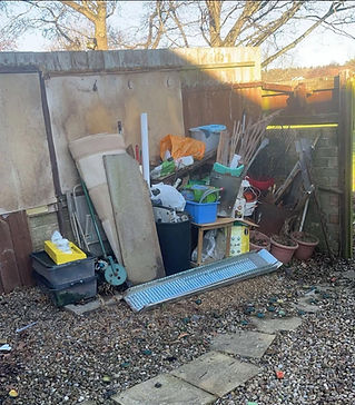 A cluttered backyard filled with various junk items, enclosed by a wooden fence