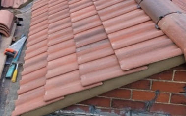 Close-up of a red tiled roof with neat rows of overlapping tiles. Tools rest nearby on the ridge