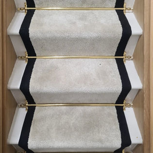 Grey stair runner with dark blue border and brass stair rods fitted on wooden stairs