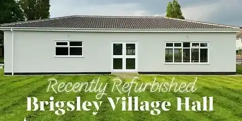 Recently Refurbished Brigsley Village Hall with light gray walls white framed windows and a green lawn