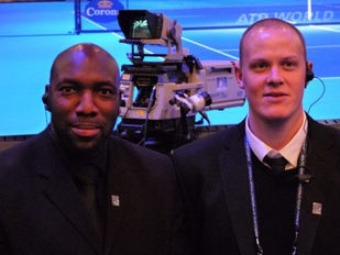 Two men in formal attire posing in front of event cameras