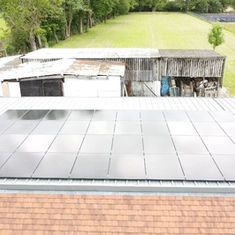 Aerial view of solar panels on a barn roof, surrounded by green fields and trees