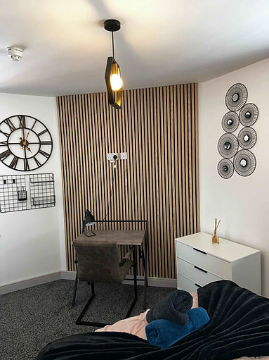 student room with a wooden slat accent wall, small desk, chair, and lamp