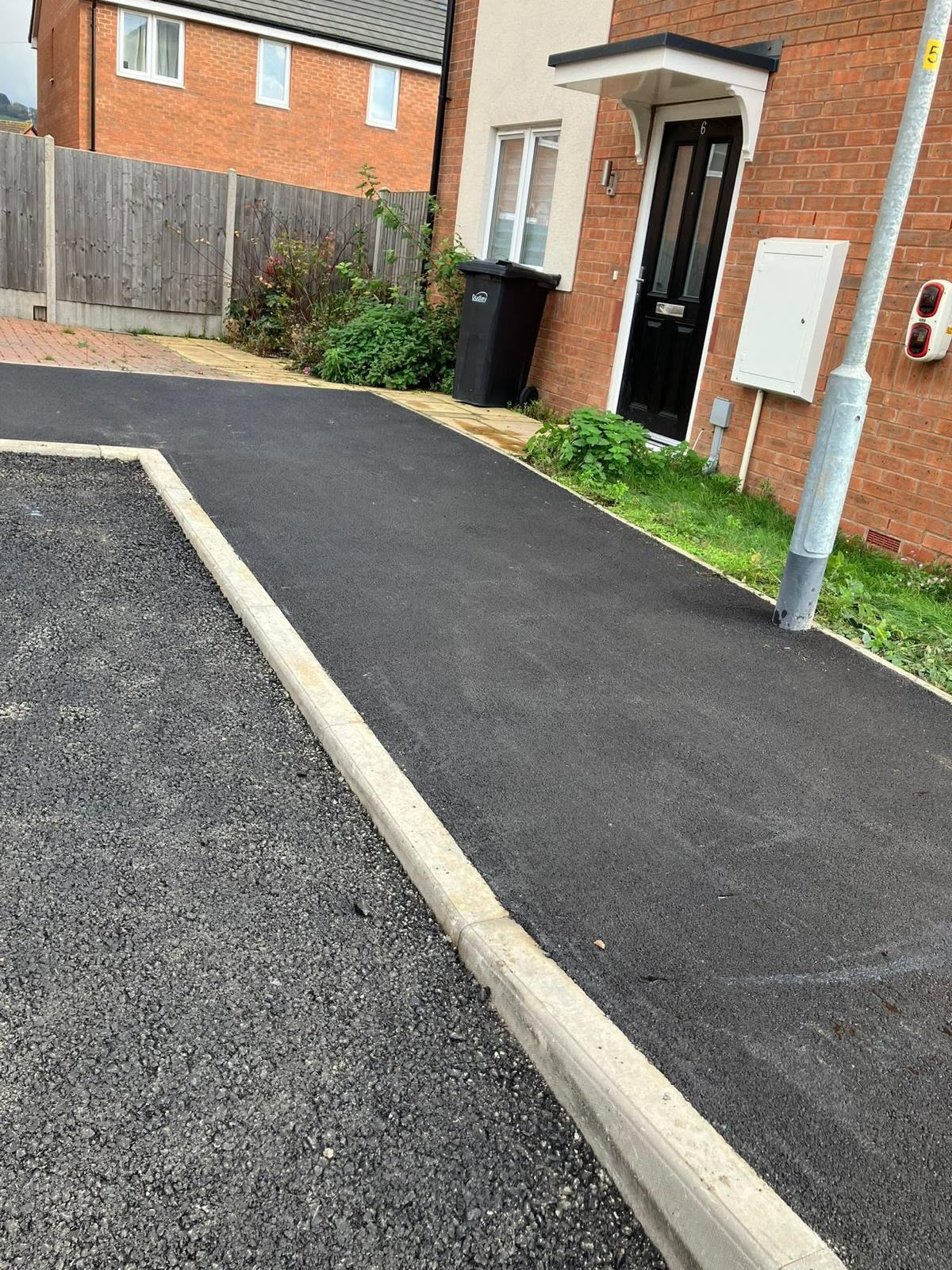 New concrete kerbs bordering a newly laid dark tarmac path
