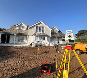 Land surveying total station on a yellow tripod at a residential house construction site under a clear blue sky