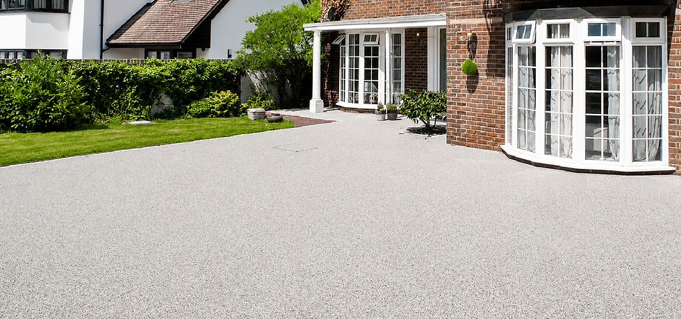 A white driveway leading to a brick wall, surrounded by greenery