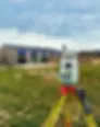 Land surveying total station on a yellow tripod in a grassy field with a building under construction