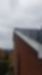 View of a red brick house roof with black tiles, under a cloudy sky. The roof edges form neat lines. 