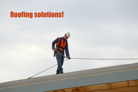 A construction worker in a safety vest and helmet stands on a roof, holding a safety line