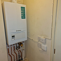 White boiler installed in a small utility space, connected to copper pipes