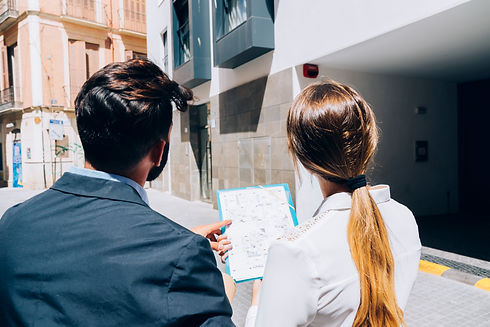 Rear view of two property surveyors reviewing plans on a clipboard outside a modern building