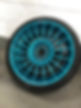 Turquoise alloy wheel with intricate spoke design, leaning against a white and gray brick wall