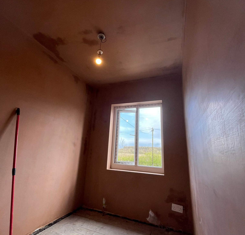A small, empty room with freshly plastered walls and an unlit single bulb hanging