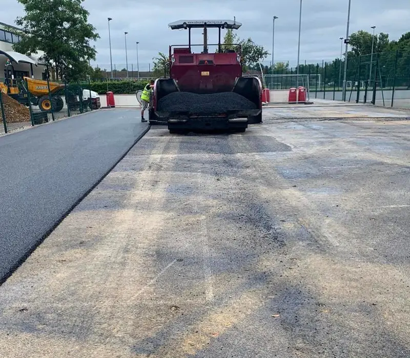 Industrial asphalt paver machine compacting a new black tarmac layer on a large construction site