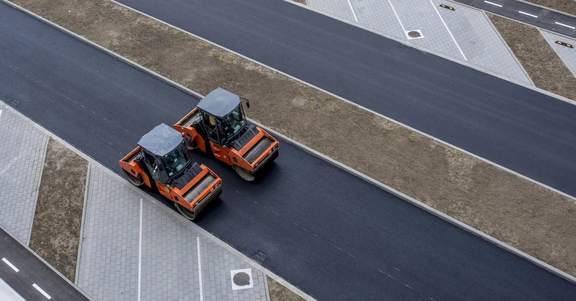 Road roller vehicle compacting a wide stretch of new grey tarmac surface