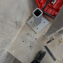 Construction site view with a gray square metallic base and a vertical hollow pipe.