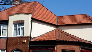 A red brick building with a prominent red-tiled roof stands beneath a clear blue sky.