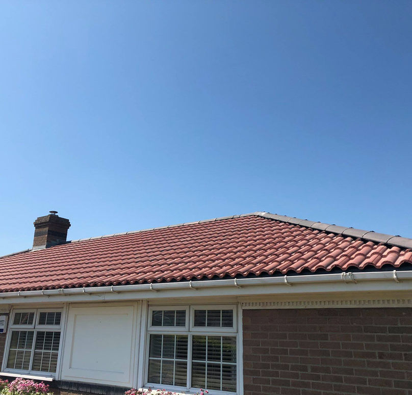 A red-tiled roof of a single-story house beneath a clear blue sky.