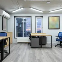 Modern office with wooden desks, blue chairs, large windows, and abstract wall art