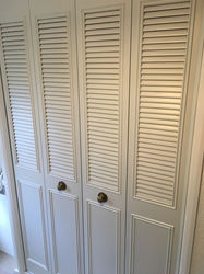 White bi-fold closet doors with louvered panels and brass knobs, casting soft shadows