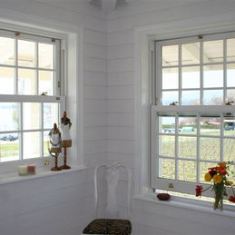 A bright corner with two white panel windows overlooking a garden