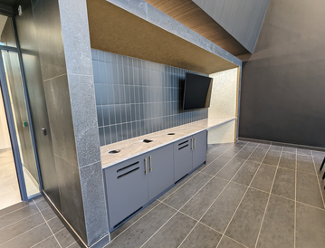 Modern office kitchenette with gray cabinets, a marble countertop, and a wall-mounted TV