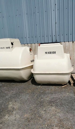 Two large white plastic septic tanks stored upright on an outdoor commercial hardstanding yard