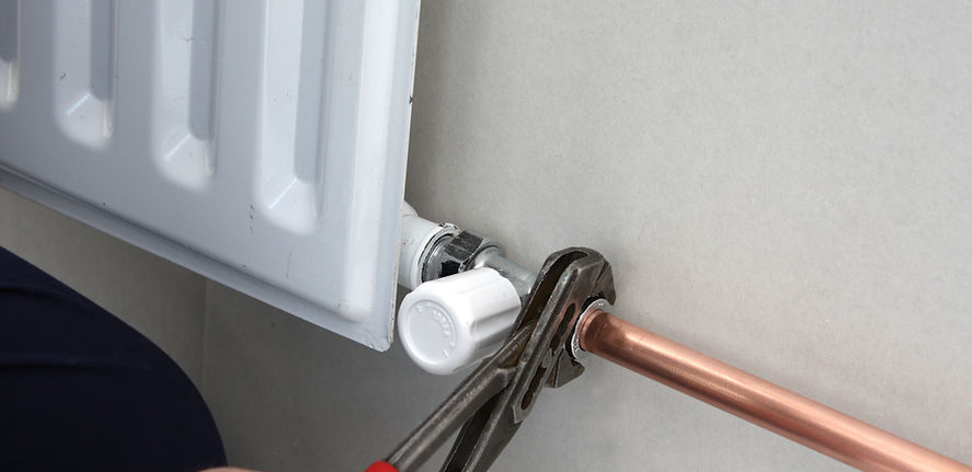 White vertical panel radiator with a copper pipe connection on a neutral-coloured wall