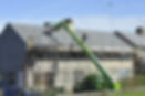 Workers are repairing the roof of a house using scaffolding and a green lift
