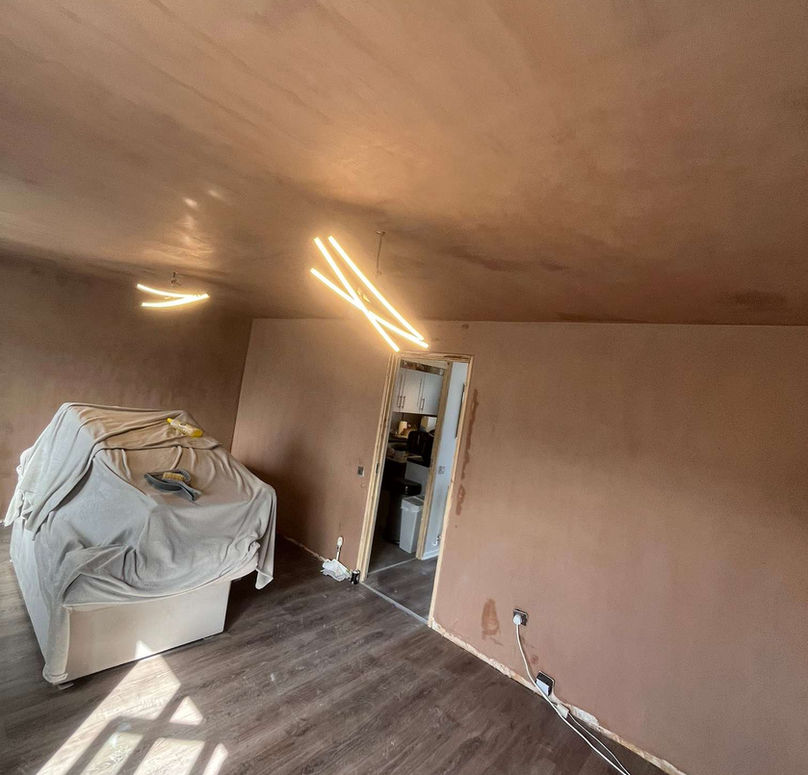 Room undergoing renovation with smooth plastered walls and exposed ceiling lights