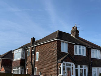Semi-detached brick house with white framed windows and chimneys under a clear blue sky