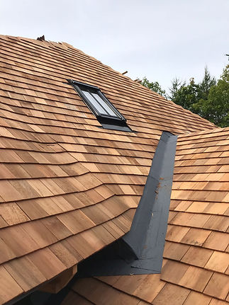 Close-up of a wooden shingle roof with a black-framed skylight. The shingles are arranged in neat